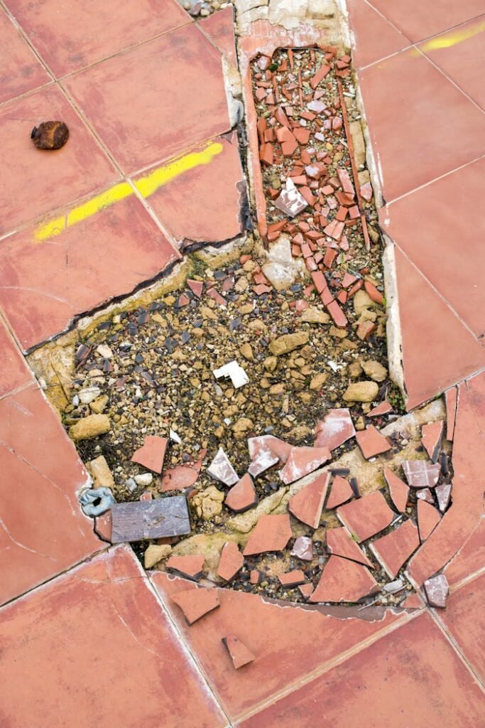 Cracked tile floor revealing underlying debris and broken materials.